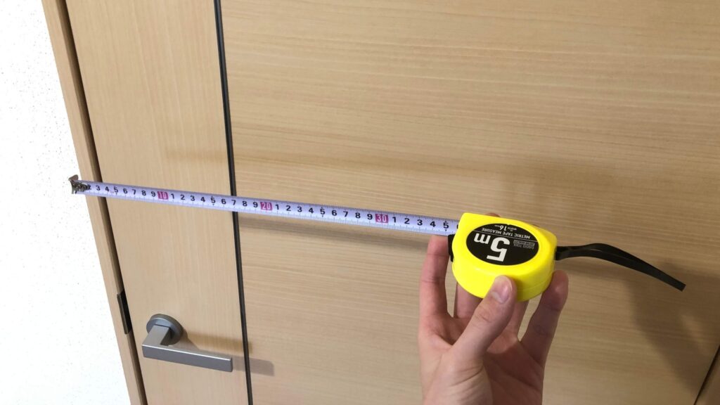 ドア前でメジャーを使いドア幅を測っている手元