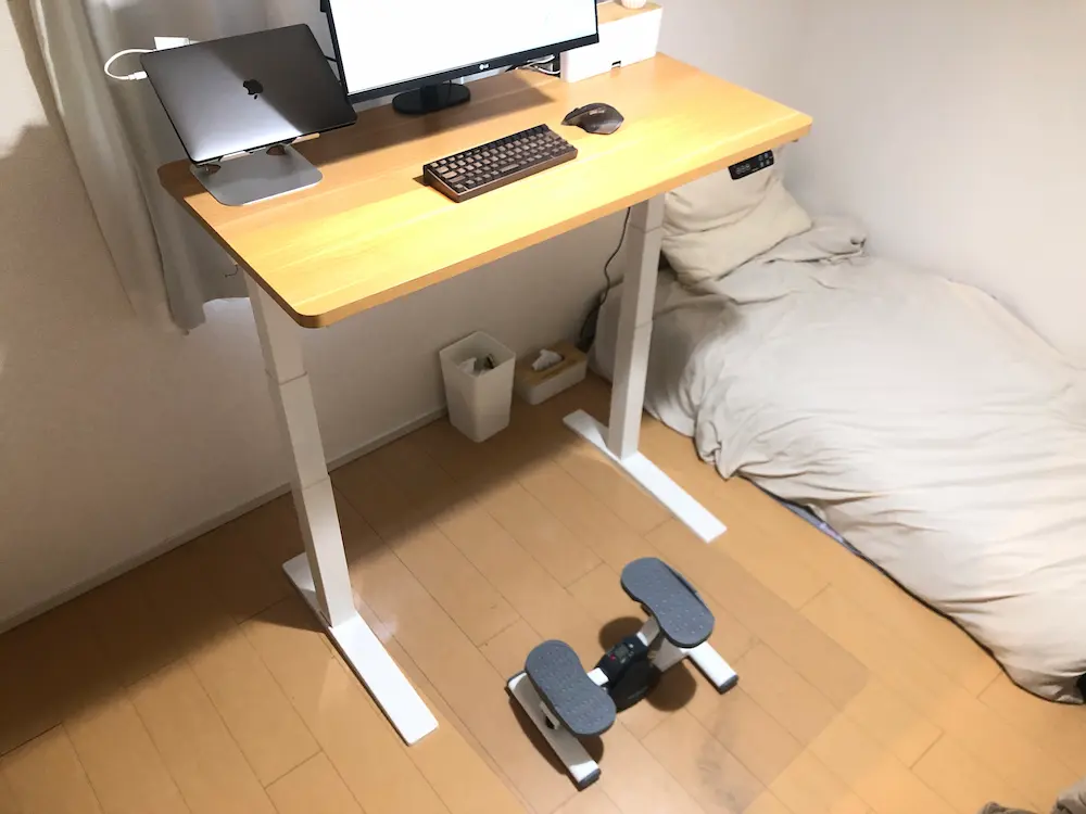 電動昇降デスクを高く設定し、足元にステッパーを置いて作業している様子。