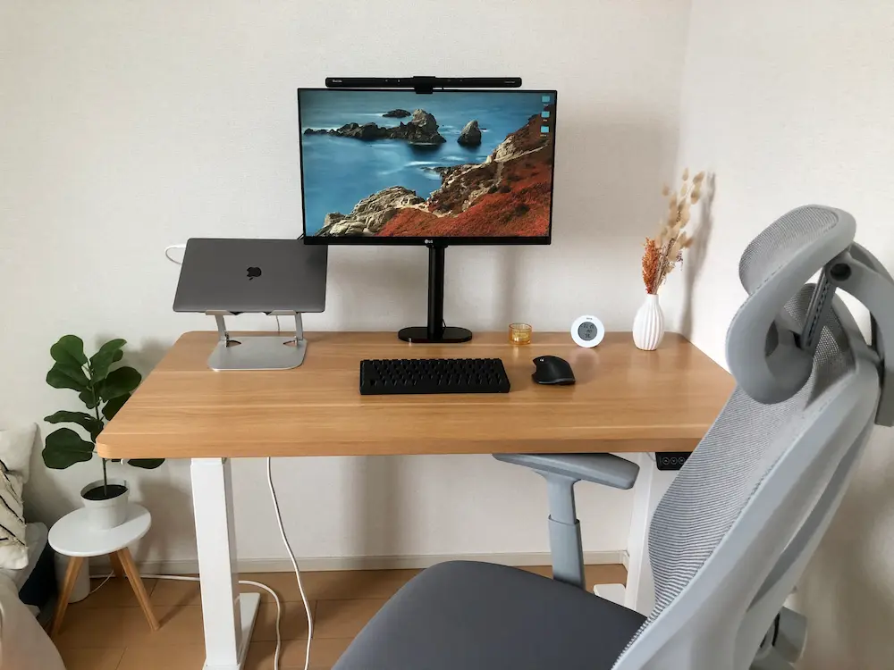 モニターアームで浮かしたディスプレイと、天板に置かれた造花によるおしゃれなデスクセットアップ