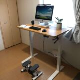 扉から見た6畳の在宅ワーク環境。電動昇降デスクとステッパーを設置し、デスク上にはコーヒー、メモ帳、観葉植物を配置している様子