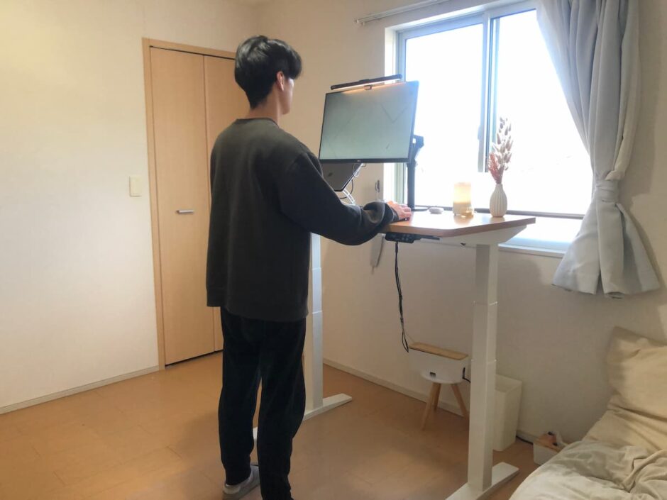 FlexiSpot E7を使って立ち作業する在宅ワーカーのデスク風景。